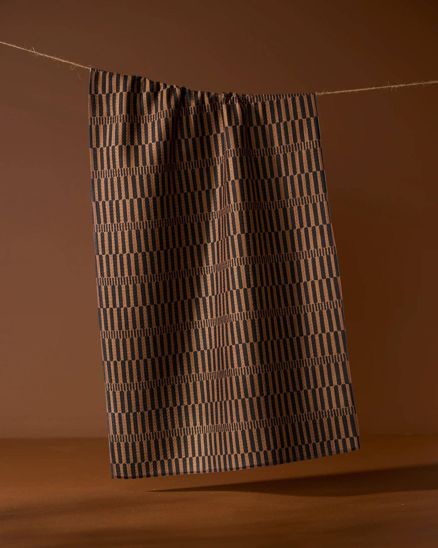 Brown and black striped tea towel hanging on a line on brown background.
