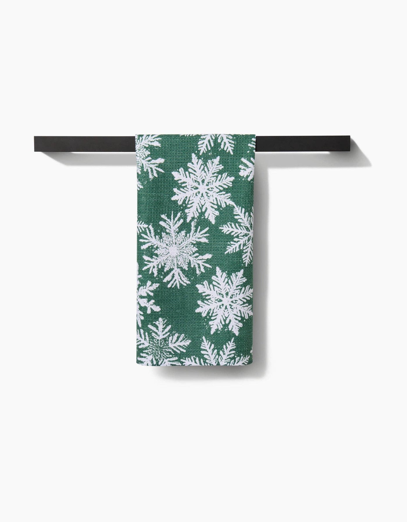Green towel with white snowflake pattern hanging on a black metal rack against a white background