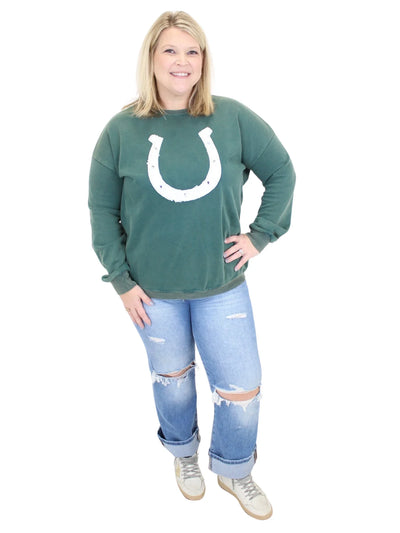 Person wearing a green sweatshirt with a horseshoe design and ripped jeans on a white background