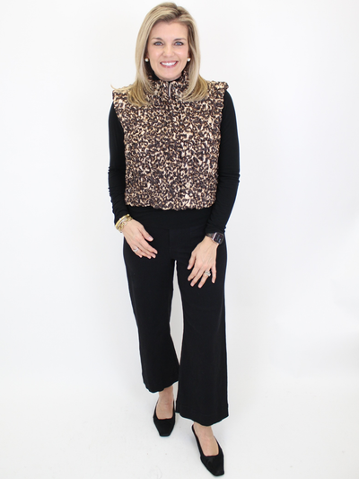 Woman wearing a leopard print vest over a black long-sleeve shirt and black pants on a white background