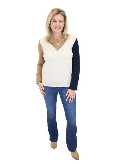 Woman wearing a cream and navy sweater with blue jeans on a white background