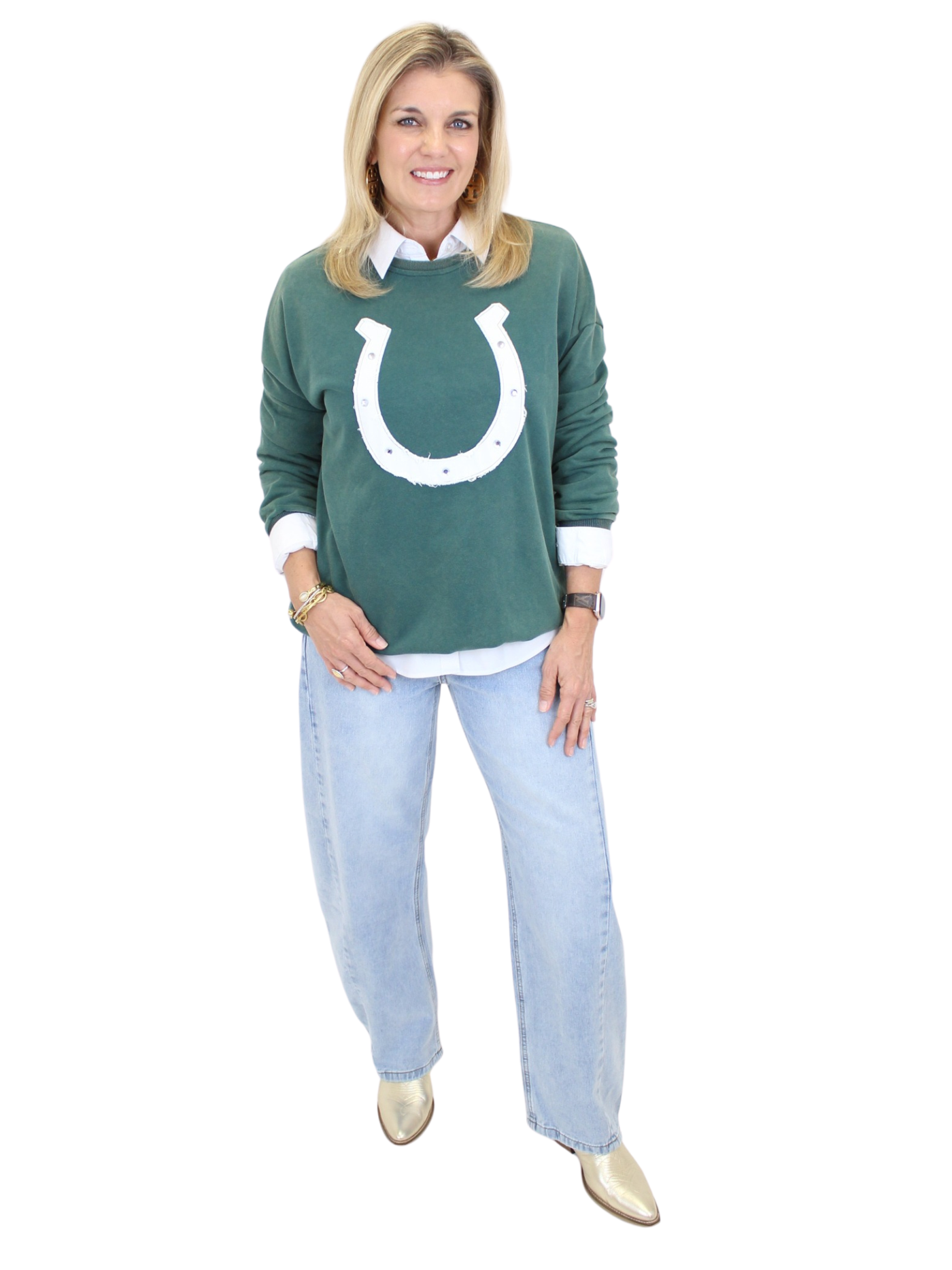 Woman wearing a green sweater with a white logo, light blue jeans, and white shoes on a white background