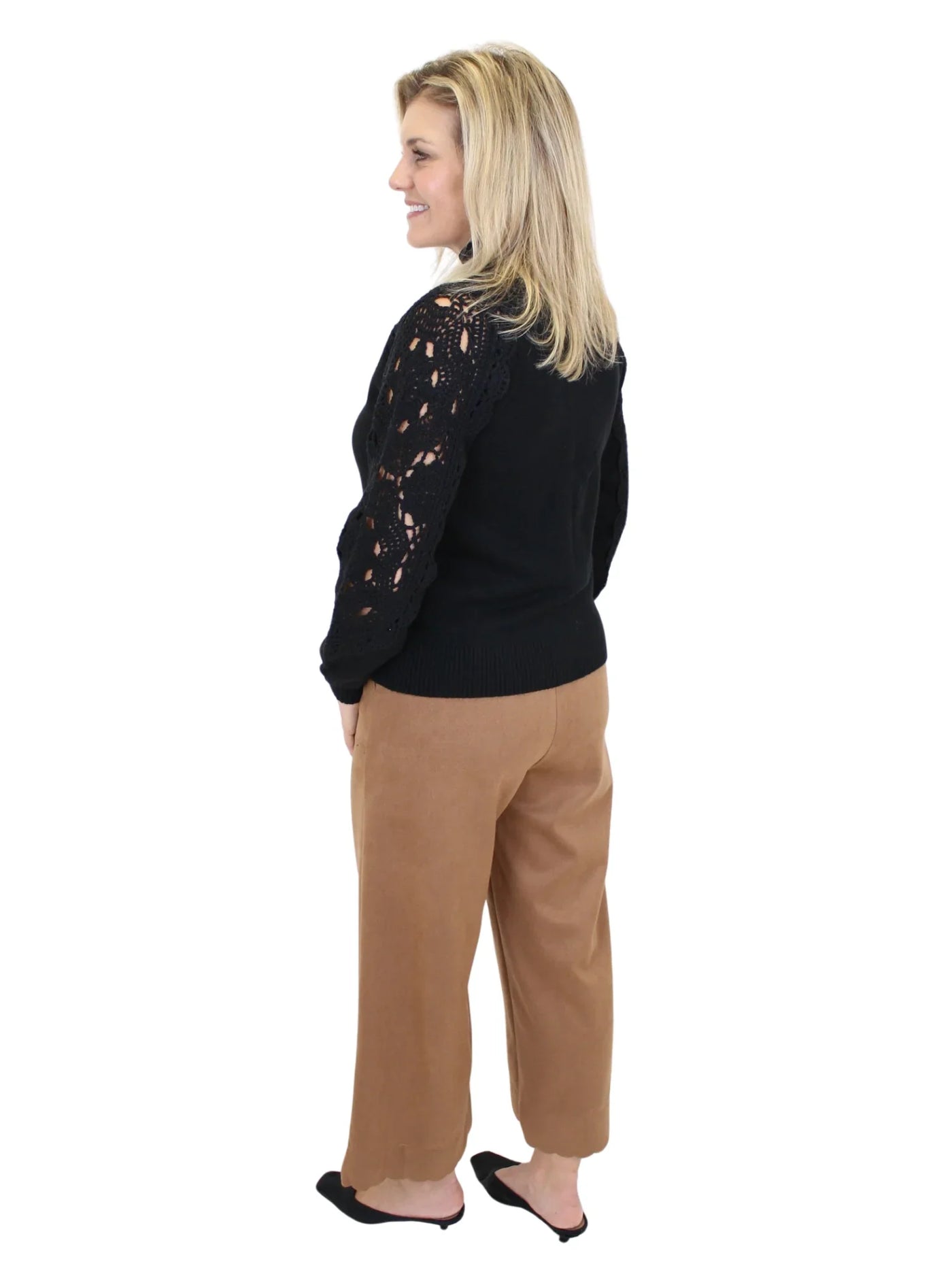 Woman wearing a black sweater with lace details and tan pants on a white background