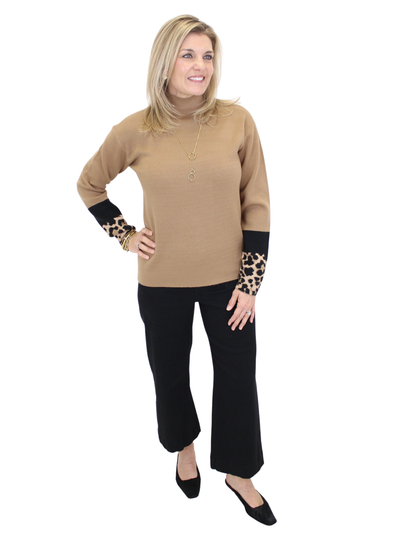Woman wearing a beige sweater with leopard print cuffs and black pants on a white background
