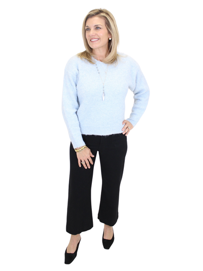 Woman wearing a light blue sweater and black pants on a white background