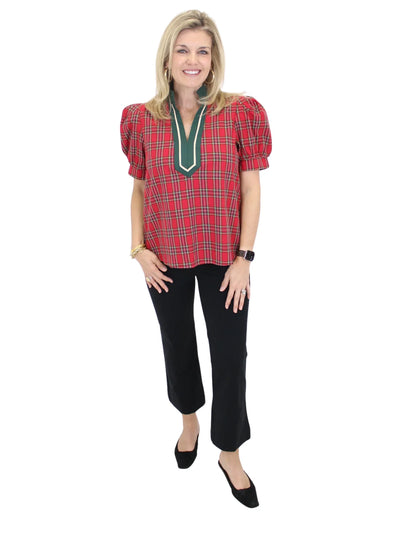 Woman wearing a red plaid blouse with green trim and black pants on a white background