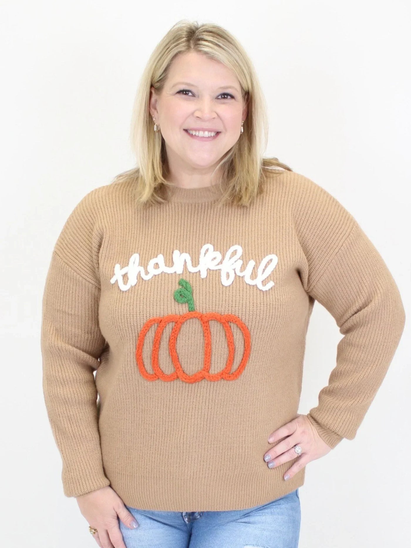 Woman wearing a brown sweater with the words thankful and a pumpkin.