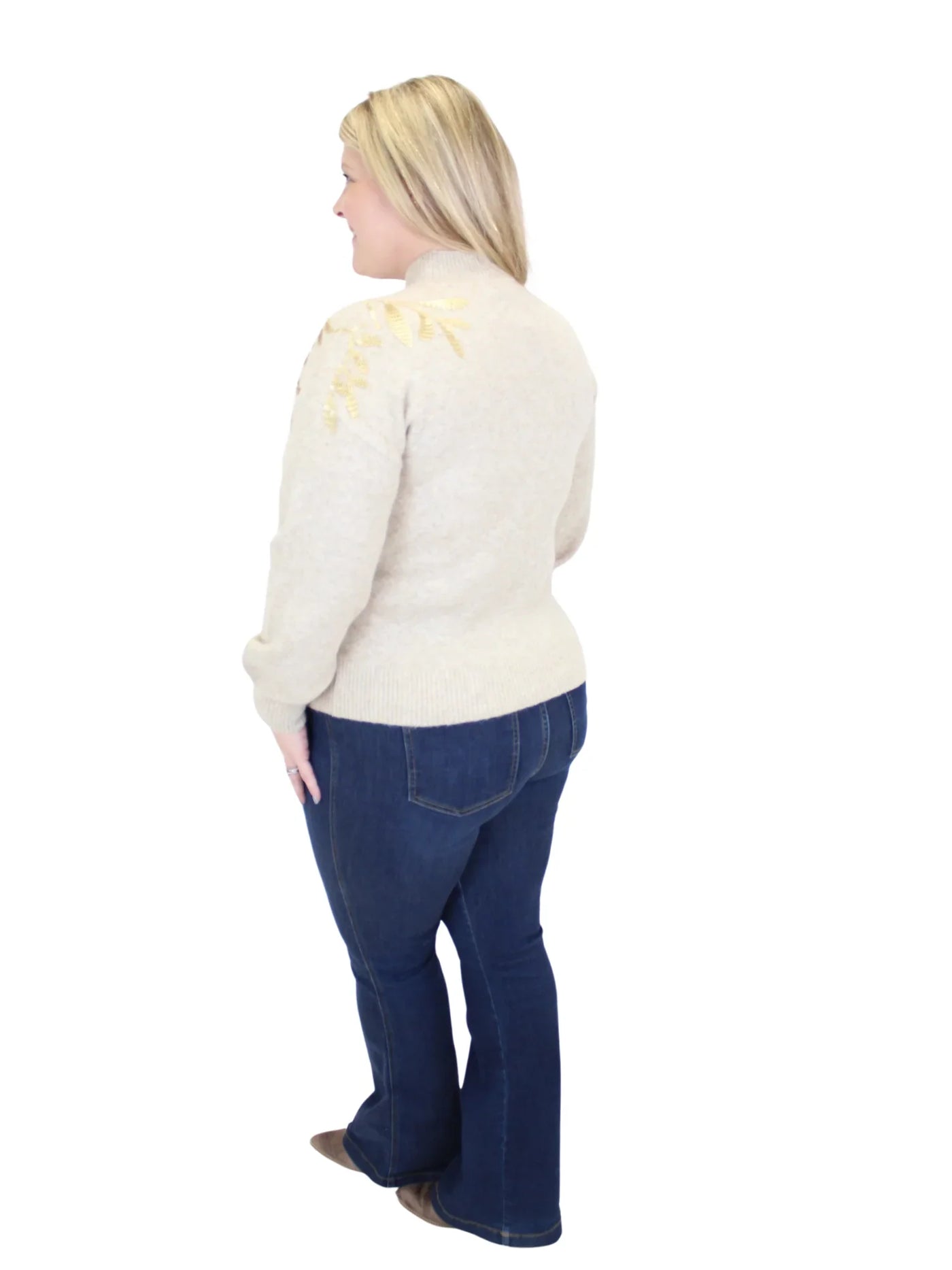 Woman wearing a cream sweater with floral embroidery and blue jeans on a white background