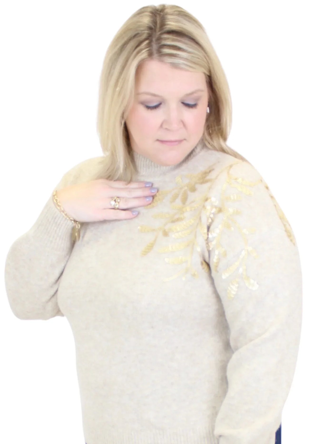 Woman wearing a beige sweater with gold embellishments on a white background