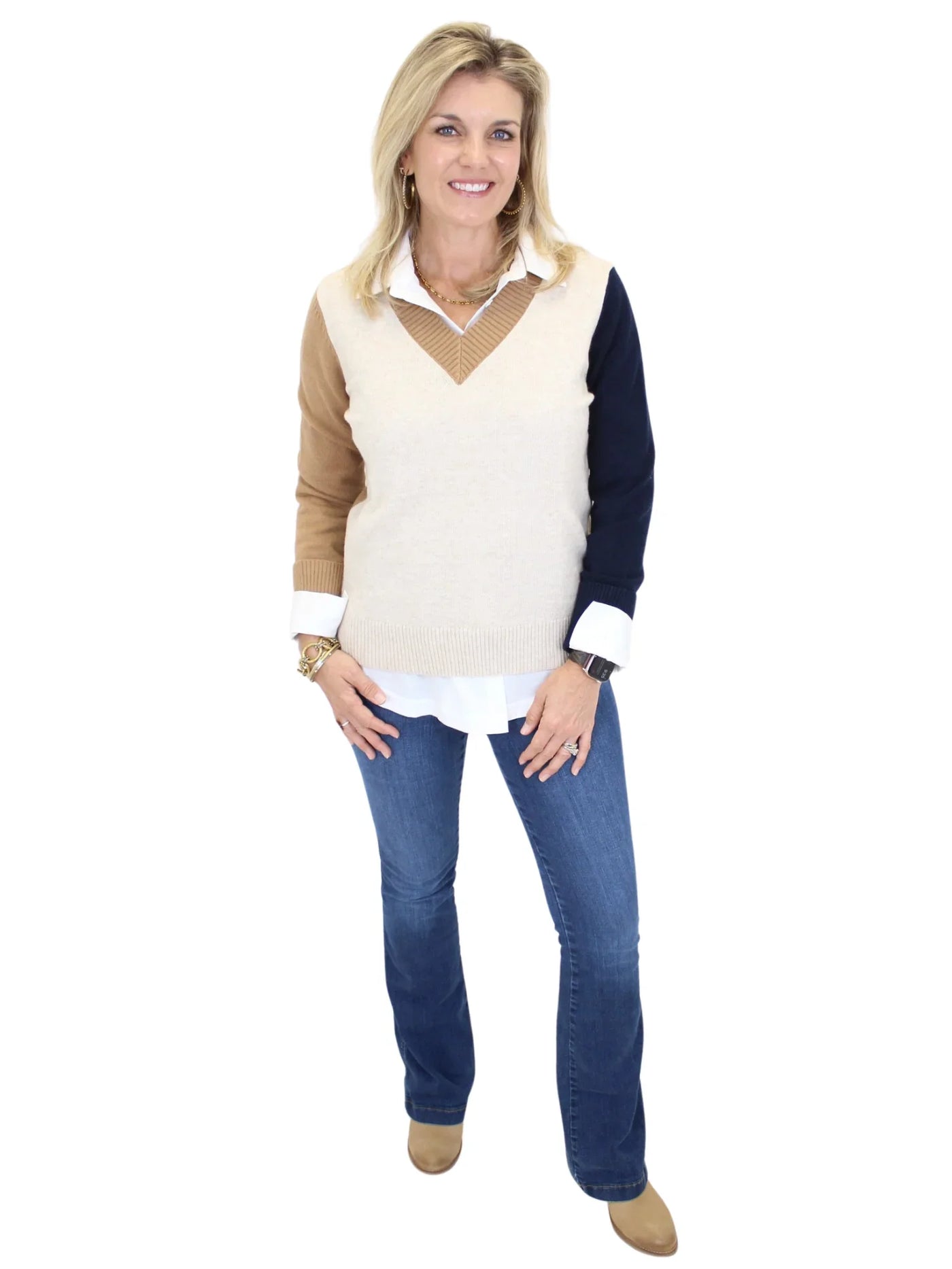 Woman wearing a  weater over a white shirt with navy sleeves, paired with blue jeans on a white background.