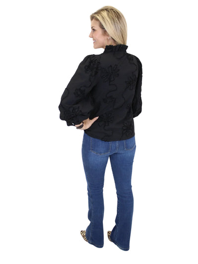 Woman wearing a black embroidered jacket and blue jeans on a white background