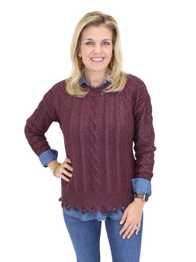 Woman wearing a maroon cable knit sweater with blue jeans on a white background