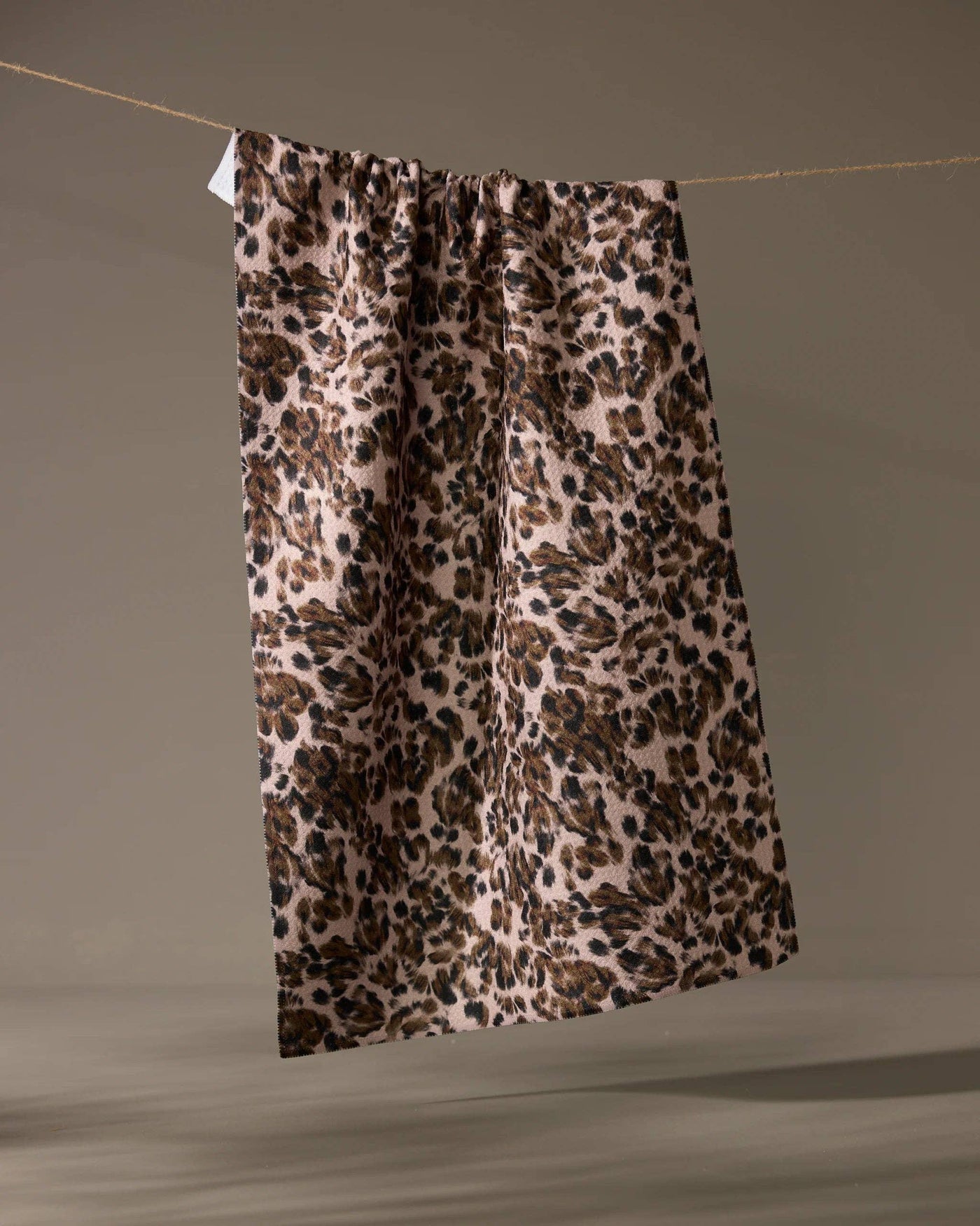 Leopard print tea towel hanging on a line against a taupe background