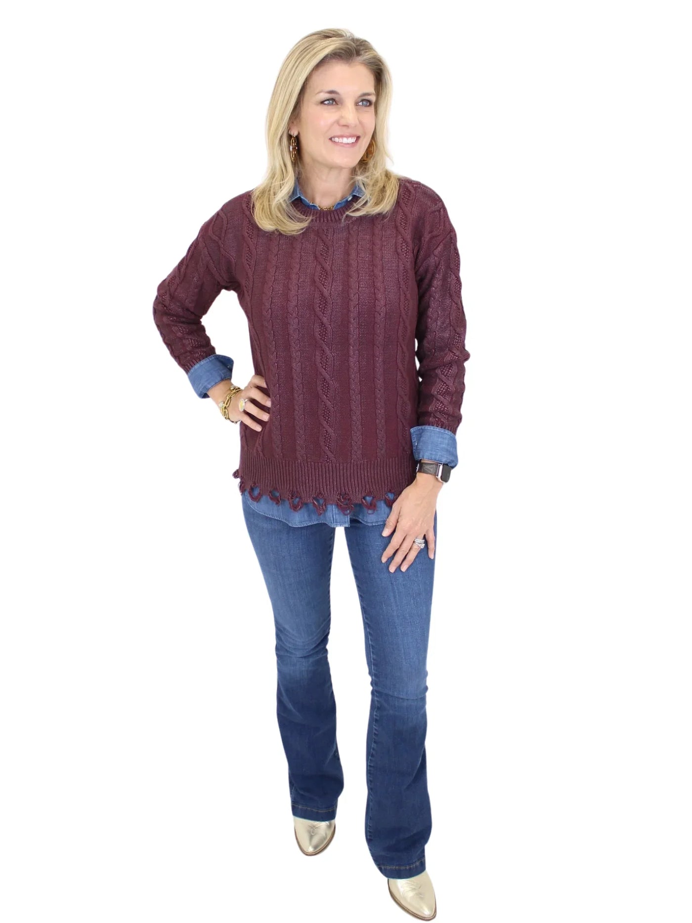 Woman wearing a burgundy cable knit sweater and blue jeans on a white background