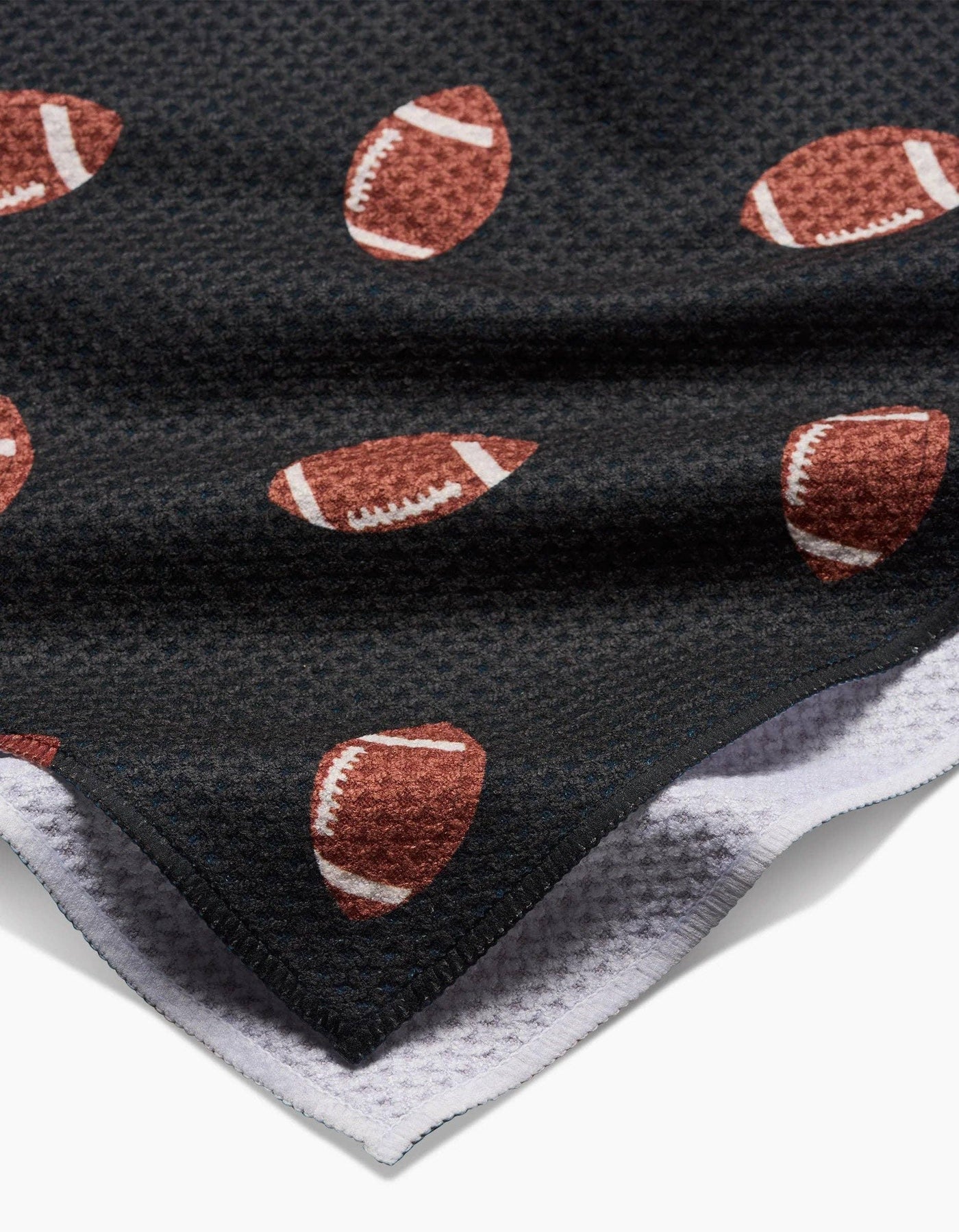 Black tea towel with brown football pattern on white background, closeup.