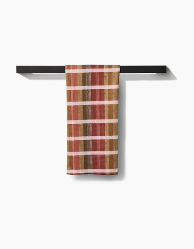 Plaid tea towel with autumnal colors on a black metal rack against a white background