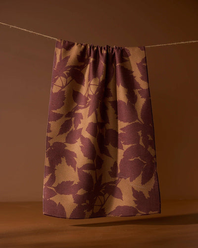 Brown leaf print tea towel hanging against a brown background