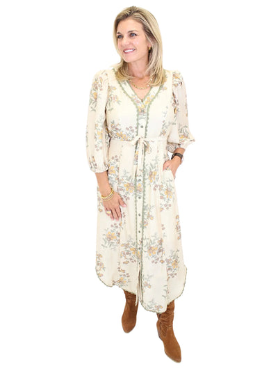 Woman wearing a long cream floral dress on a white background, front.