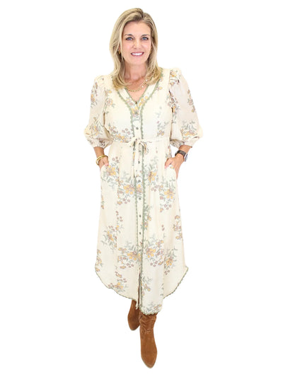 Woman wearing a long cream floral dress on a white background, front.