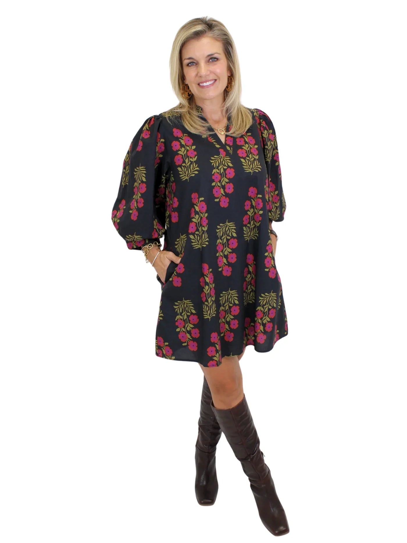 Model wearing black dress with pink flowers and knee-high boots on white background, angled front.