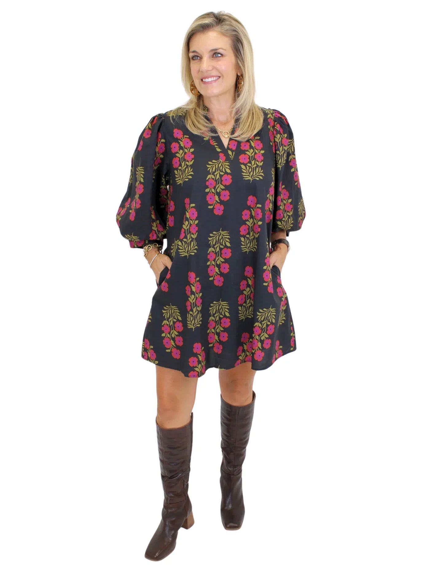 Model wearing black dress with pink flowers and knee-high boots on white background, front.