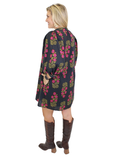 Model wearing black dress with pink flowers and knee-high boots on white background, back.