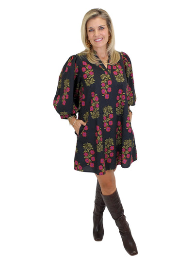 Model wearing black dress with pink flowers and knee-high boots on white background, angled front.