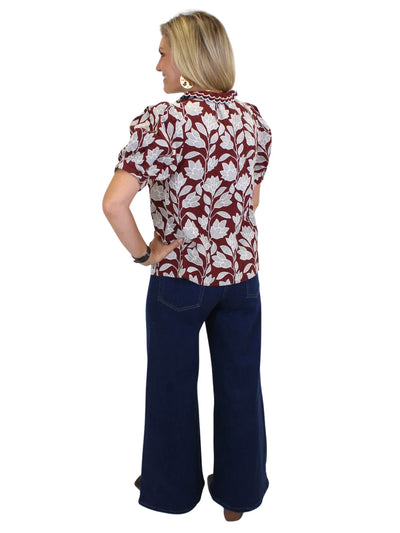 Model wearing burgundy floral top with flared jeans on white background, back.