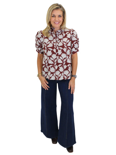 Model wearing burgundy floral top with flared jeans on white background, front