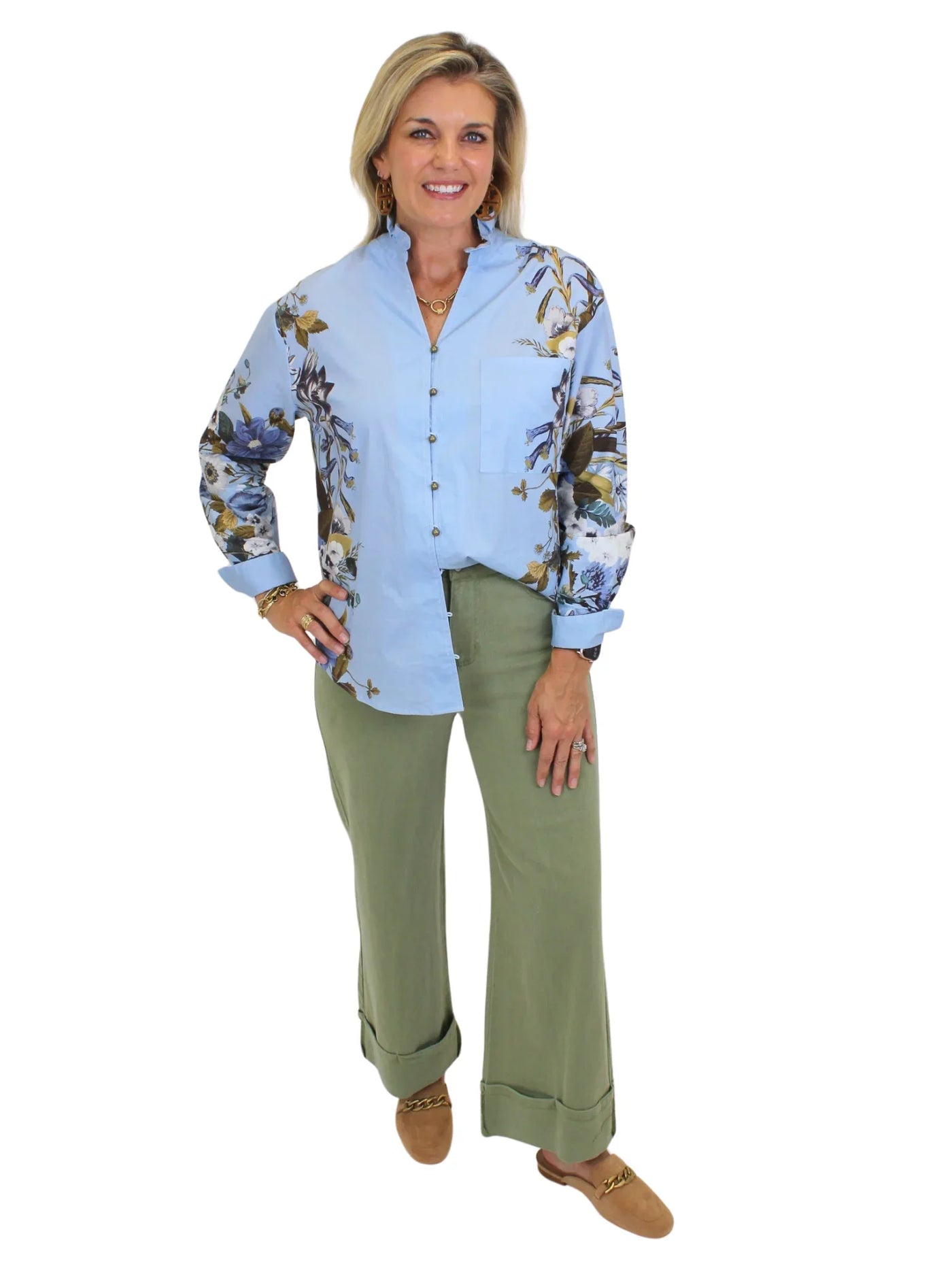 Model wearing blue botanical print button down top with green pants on white background, front.