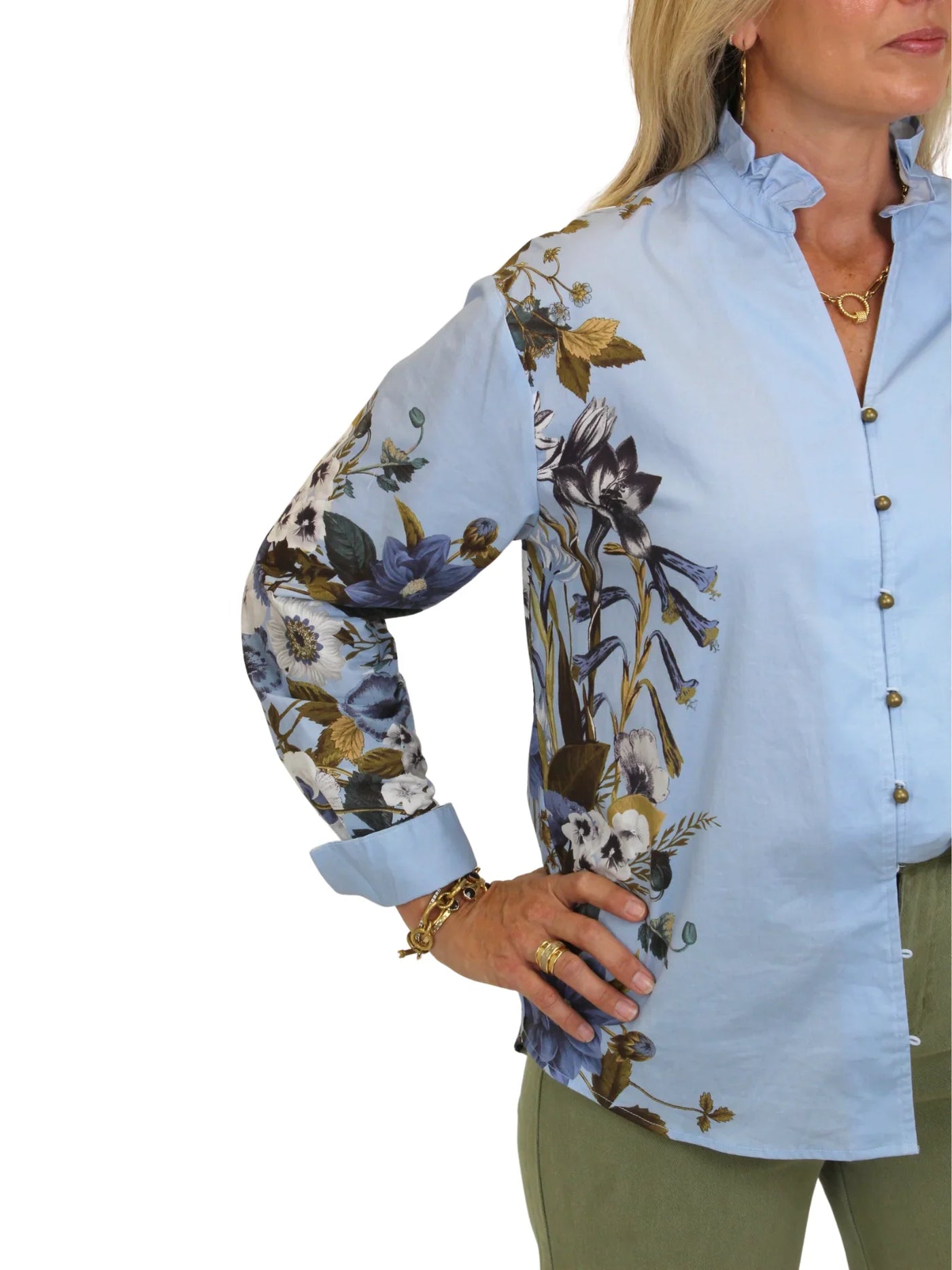 Model wearing blue botanical print button down top with green pants on white background, closeup side.