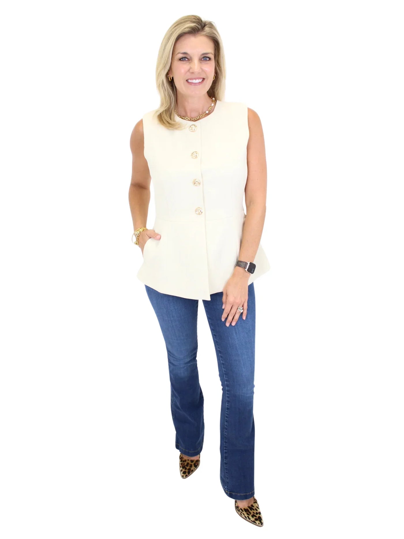 Woman wearing a cream sleeveless vest top and blue jeans on a white background, full view