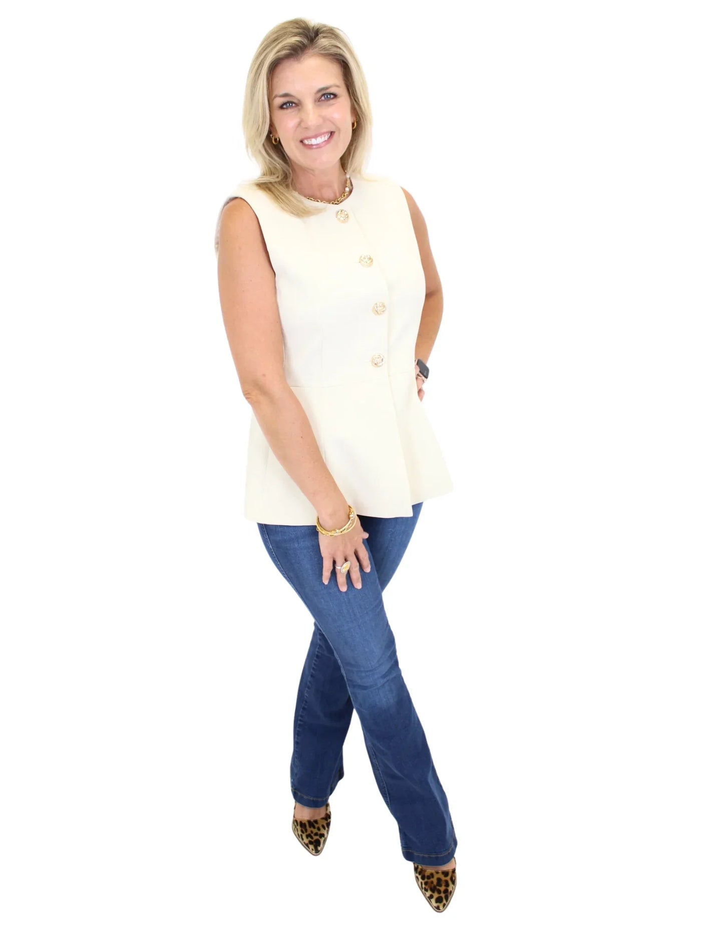 Woman wearing a cream sleeveless vest top and blue jeans on a white background, side.