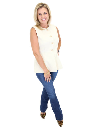 Woman wearing a cream sleeveless vest top and blue jeans on a white background, side.