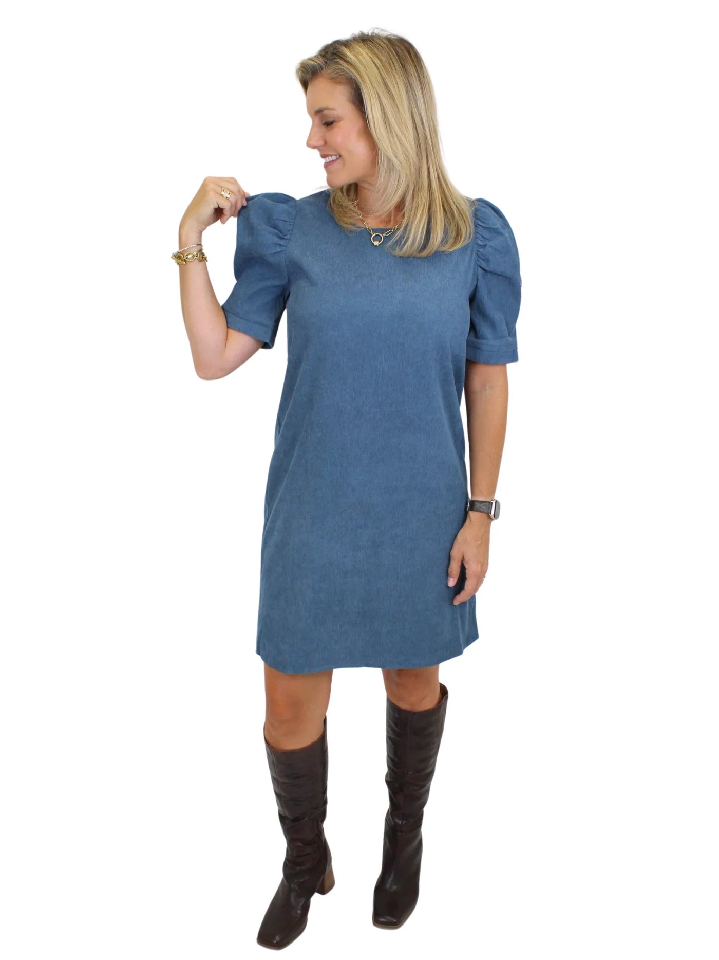 Model wearing a blue dress with puffed sleeves and brown knee-high boots on a white background, front.
