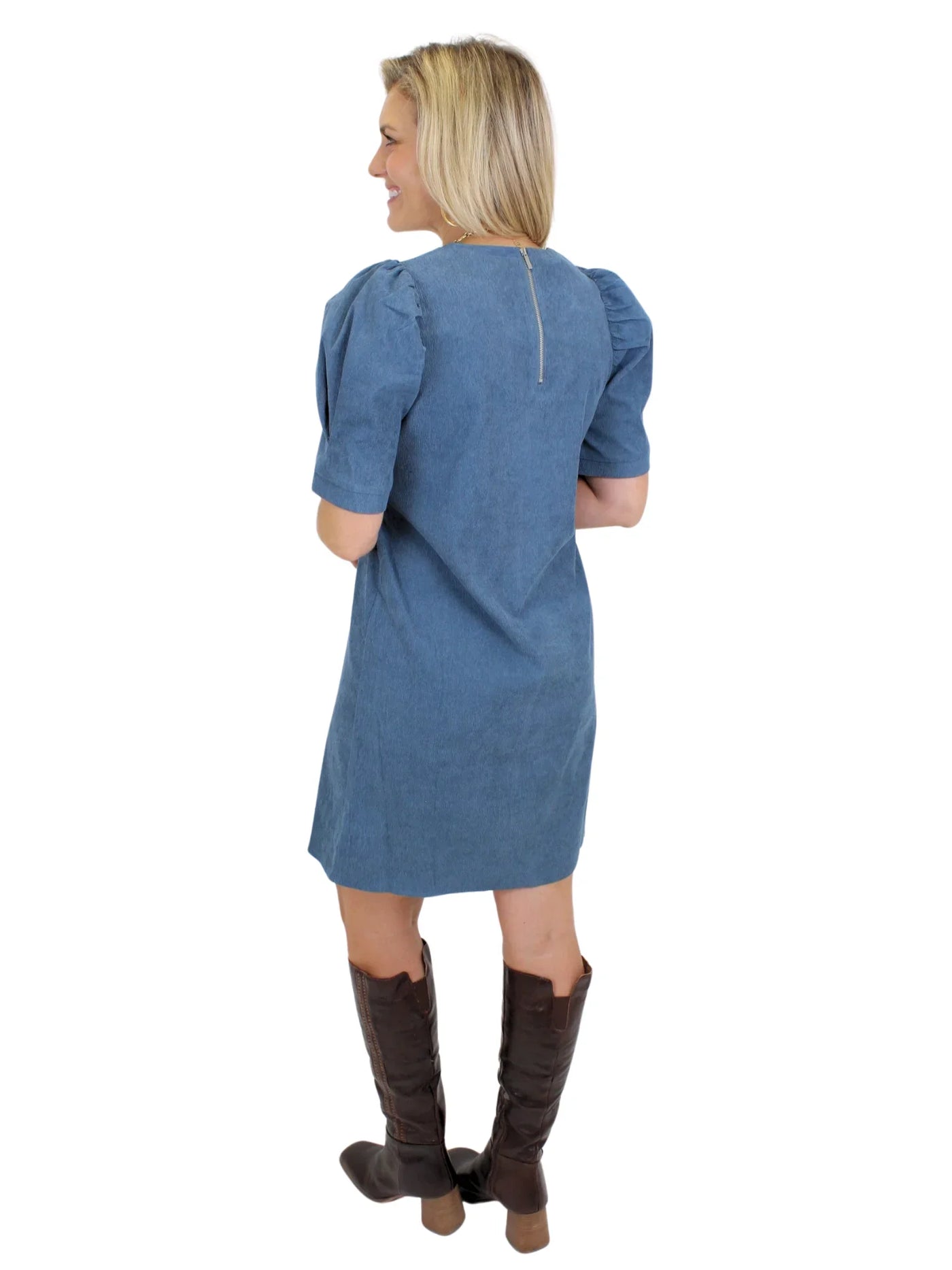 Model wearing a blue dress with puffed sleeves and brown knee-high boots on a white background, back.