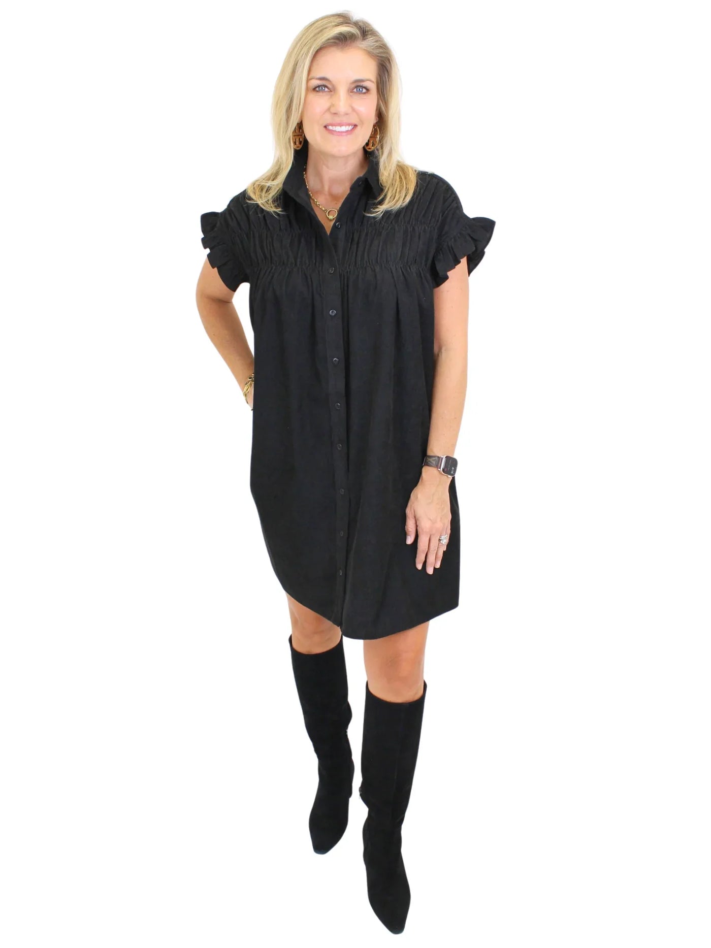 Model wearing black corduroy shirt dress with black boots on white background, front.