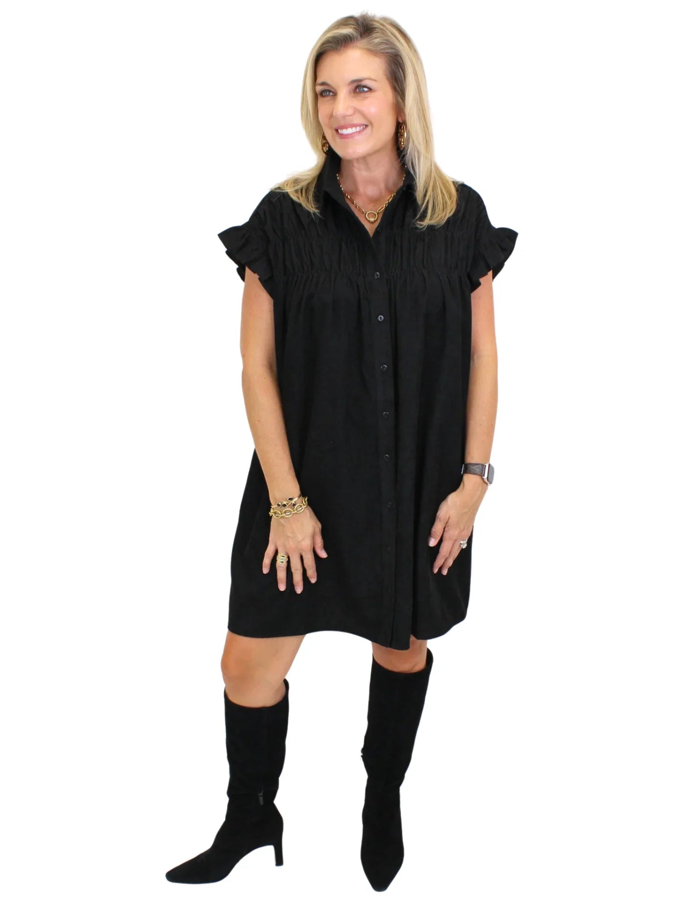 Model wearing black corduroy shirt dress with black boots on white background, side.