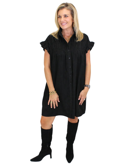 Model wearing black corduroy shirt dress with black boots on white background, side.