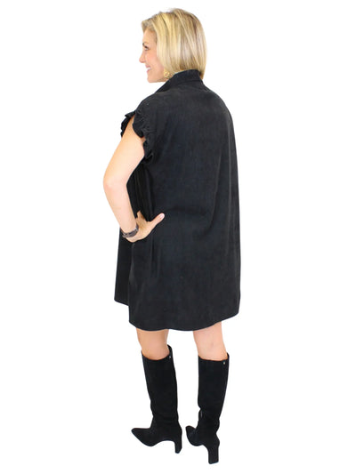 Model wearing black corduroy shirt dress with black boots on white background, back.