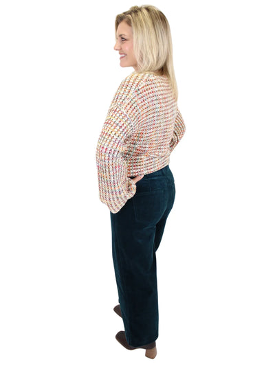 Woman wearing a multicolor sweater and dark teal corduroy jeans on a white background, back