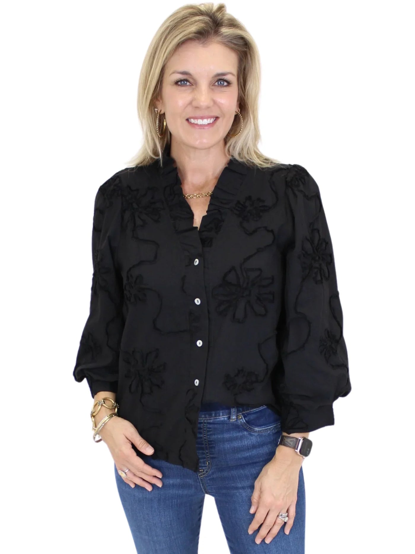 Woman wearing a black floral embroidered blouse and blue jeans on a white background