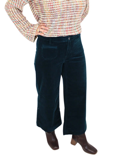 Person wearing a multicolored sweater and dark teal corduroy pants on a white background.