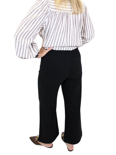 Woman wearing a striped shirt and black pants on a white background, closeup back.