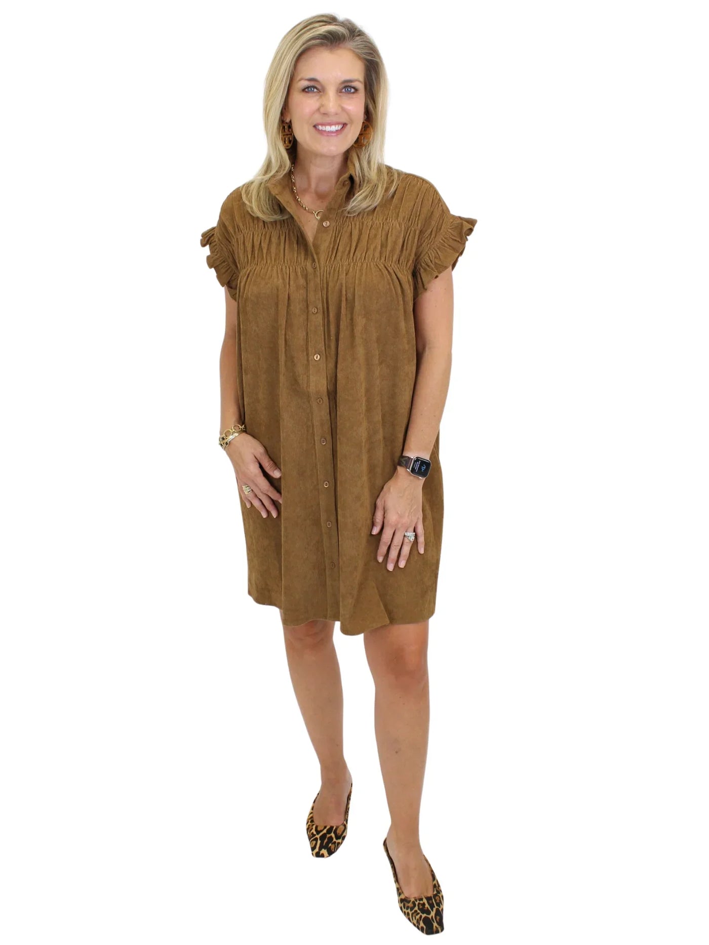 Model wearing tan corduroy gathered shirt dress and leopard mules on white background, front.