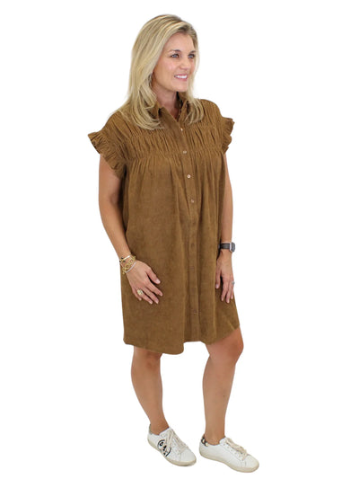 Model wearing tan corduroy gathered shirt dress and white sneakers on white background, side.
