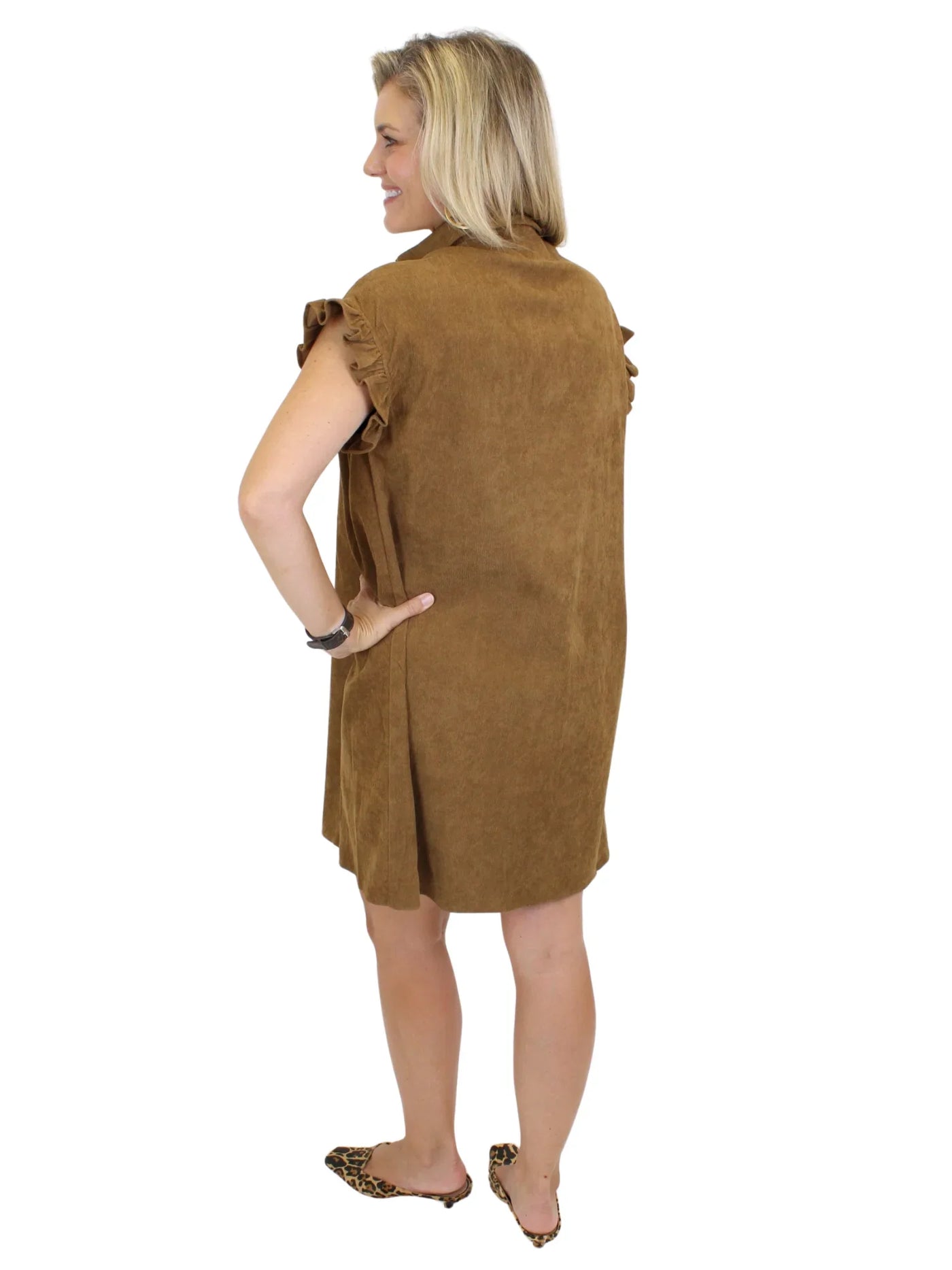 Model wearing tan corduroy gathered shirt dress and leopard mules on white background, back.