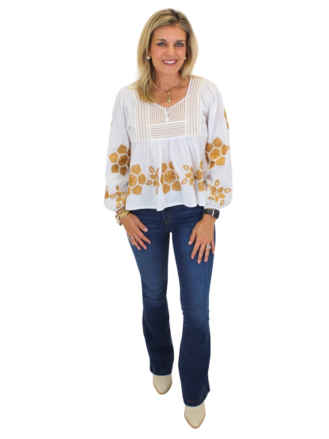 Model wearing embroidered white blouse with jeans on white background, front.