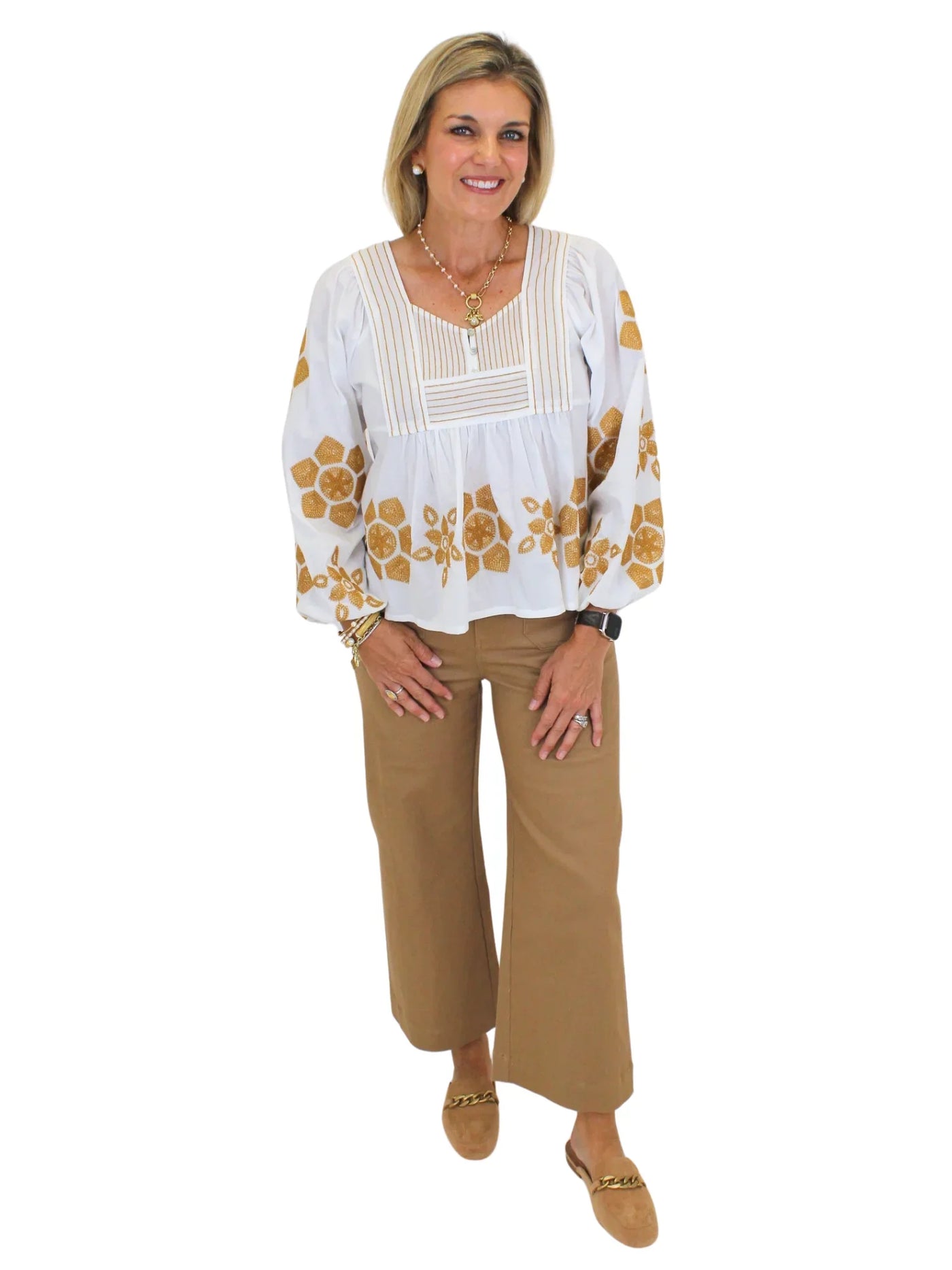 Model wearing tan embroidered white babydoll blouse and tan pants on white background, front.