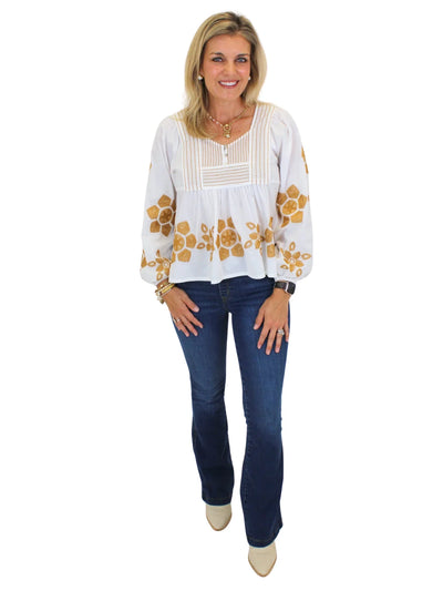 Model wearing embroidered white blouse with jeans on white background, front.